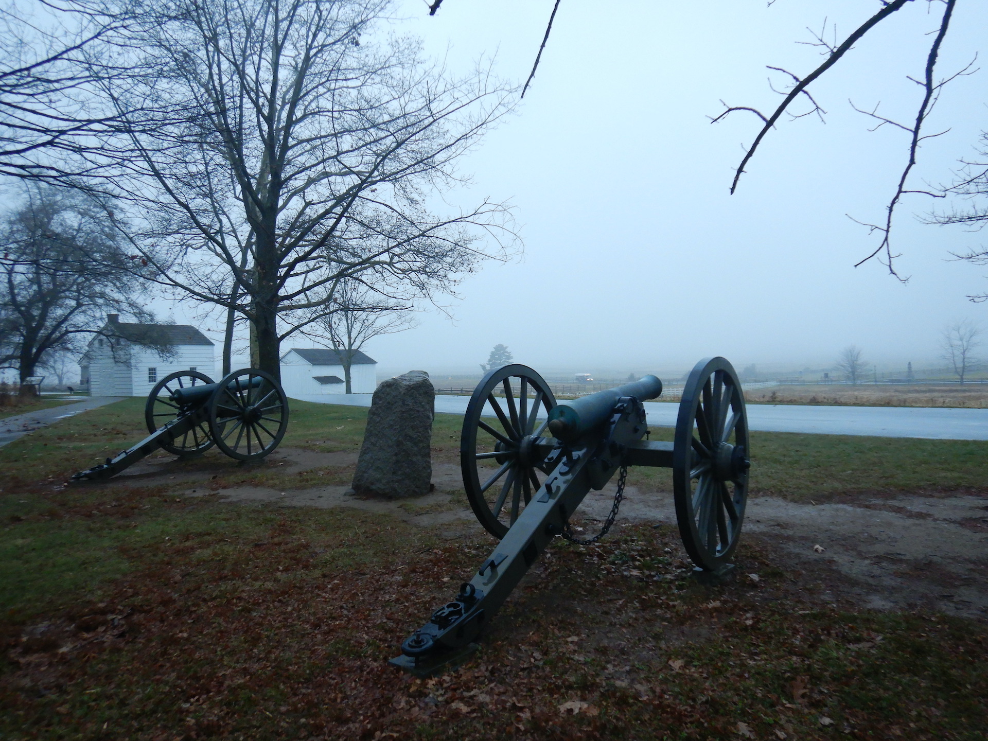 U.S. Civil War cannons face away toward horizon. Deep overcast skies and bare trees fill the scene.