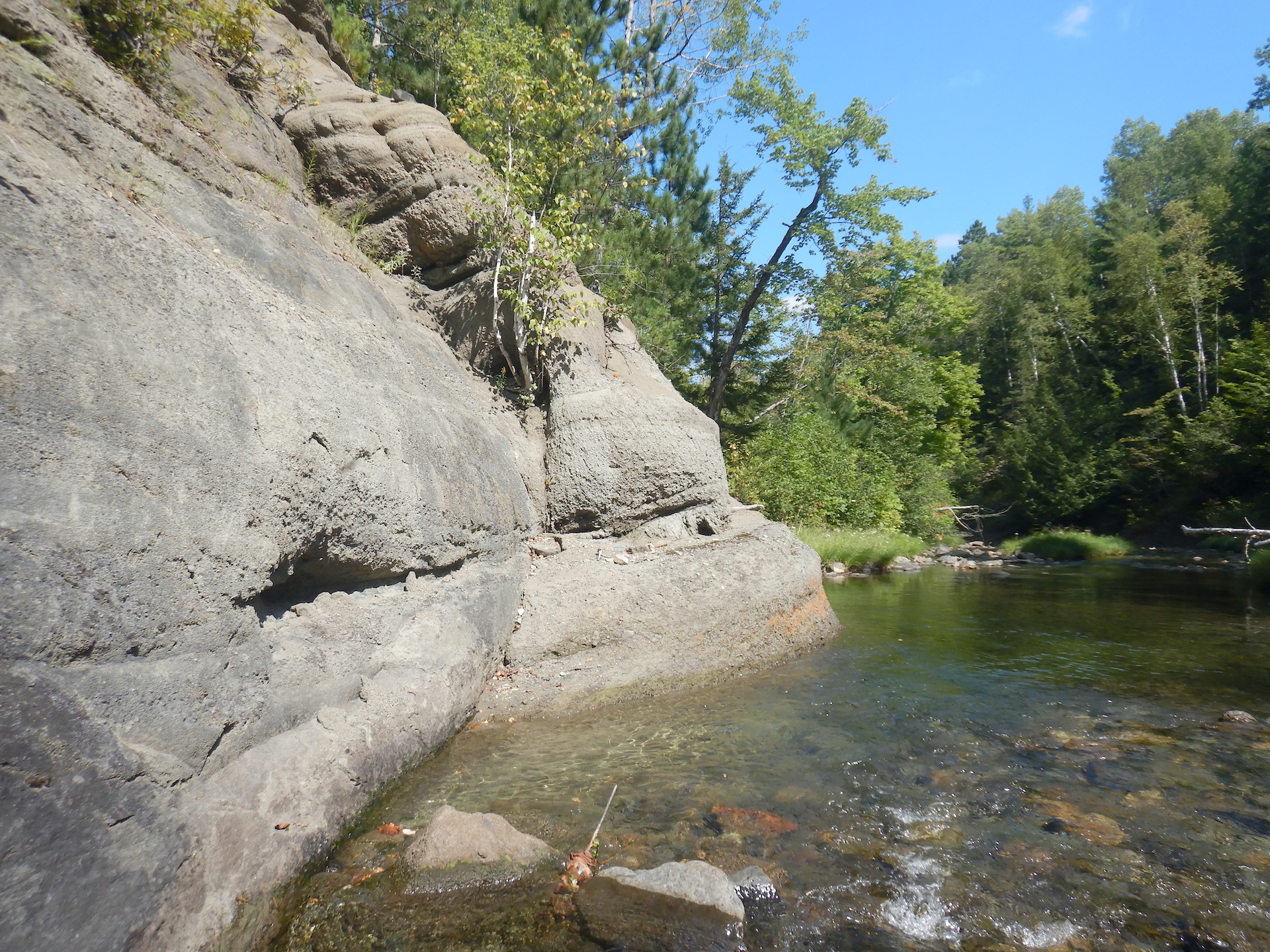 Steam flowing past a wall of gray rock. The rock wall is at left. The stream flows from lower right to center right.