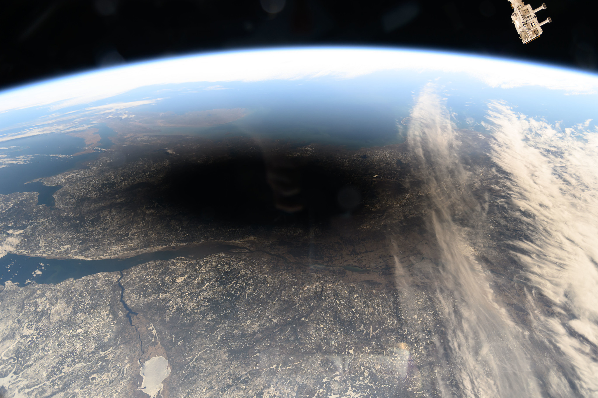 View of Earth from ISS. Atmosphere is mostly clear. A dark shadow blocks the landscape in the center of the photo.